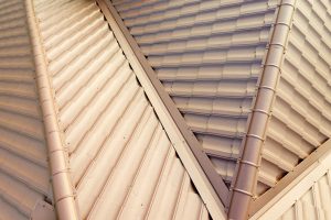 Detail of a house roof surface covered with brown metal tile sheets.